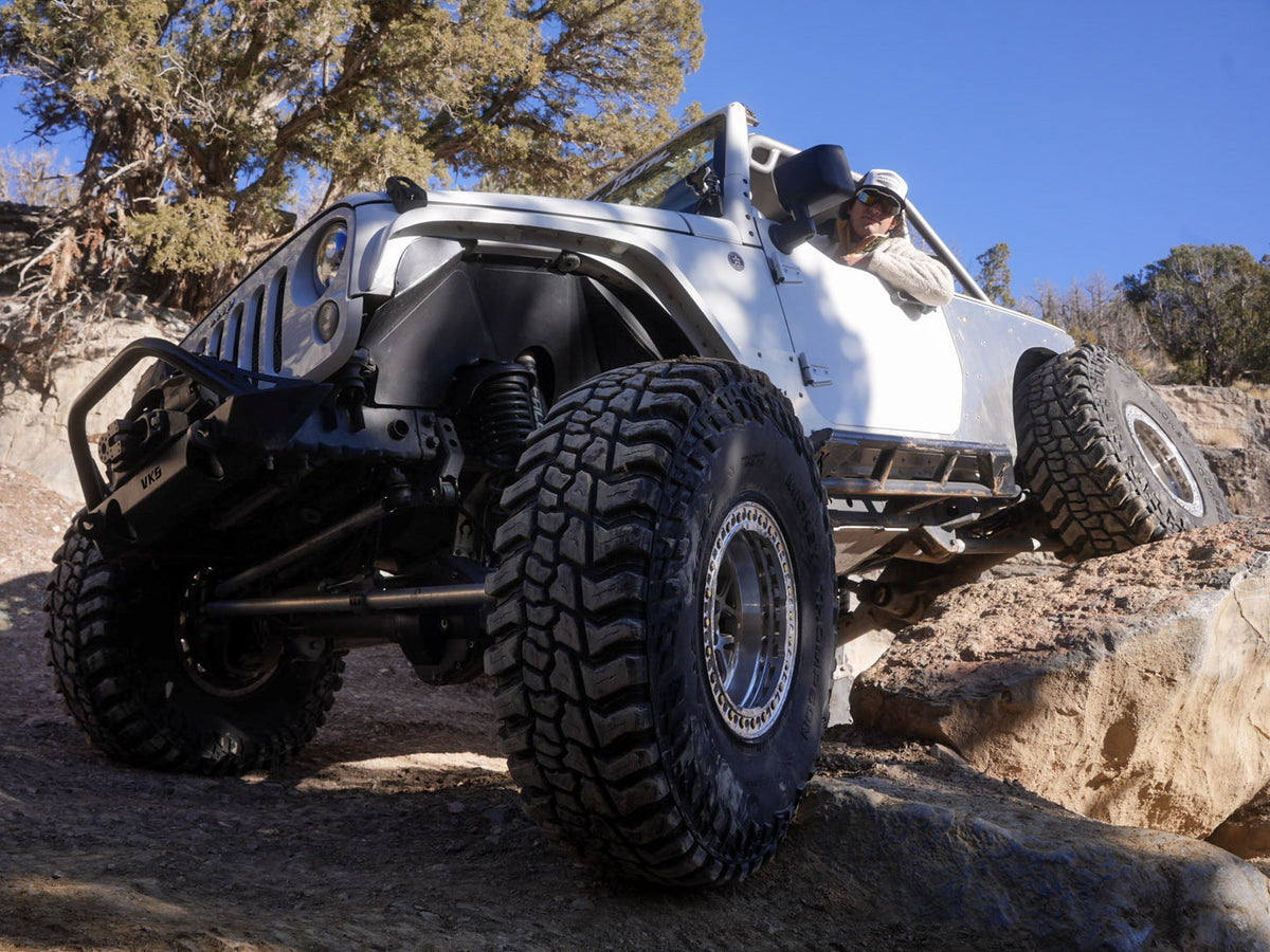 White Jeep climbing a rocky desert trail on large off-road tires