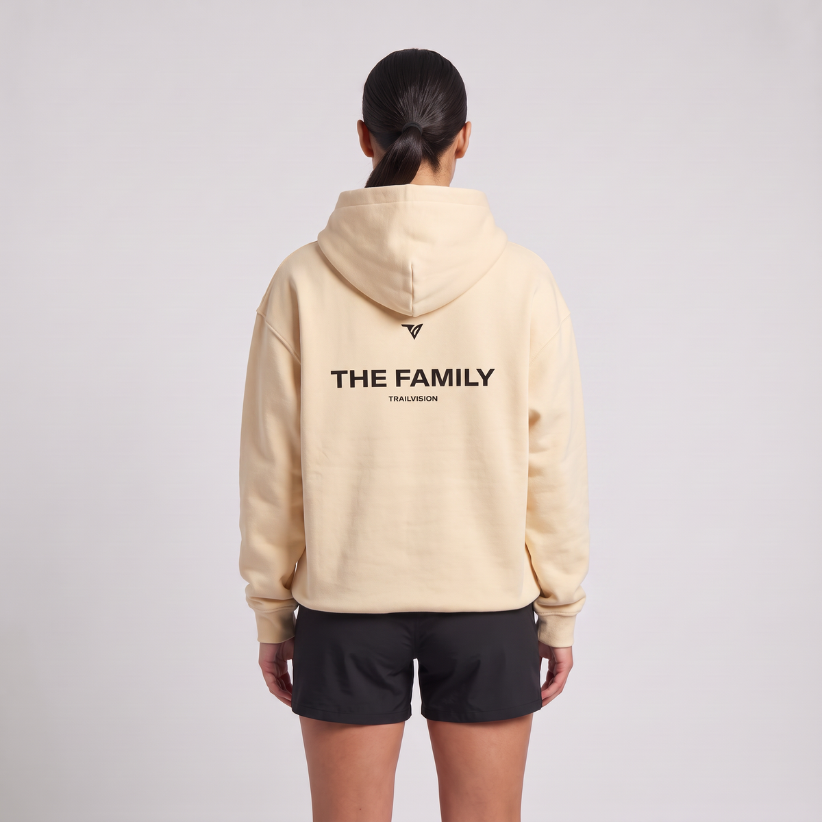 Female model wearing The Family Hoodie in Mild Apricot, rear view with large back print