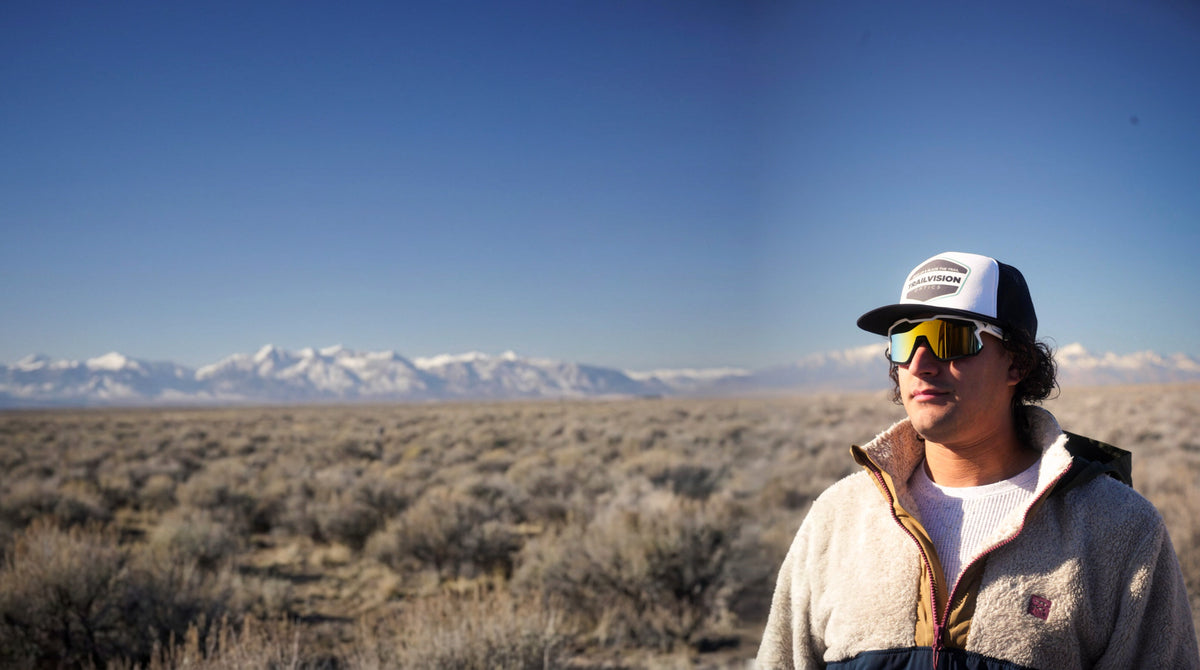 Rider in Trailvision shield sunglasses and trucker cap in the high desert with snowy mountains